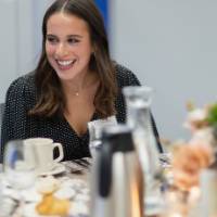 Young woman smiling at someone seated at her table
